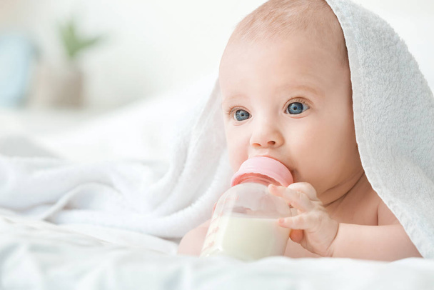Portret uroczego maluszka pijącego mleko z butelki na łóżku - Zdjęcie, obraz