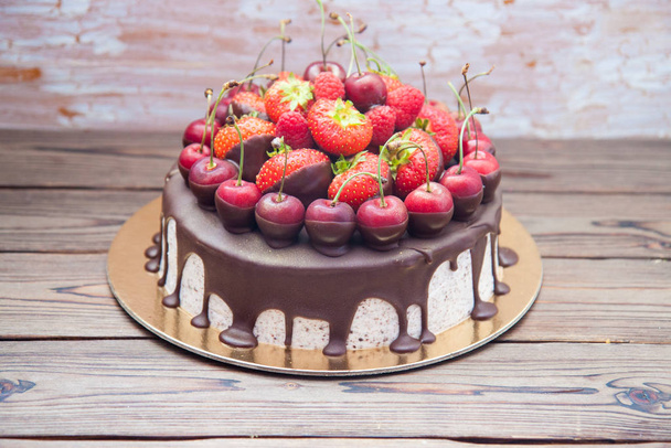 Cheesecake with melted chocolate, fresh strawberries, cherries and raspberries on wooden background.  - Fotografie, Obrázek
