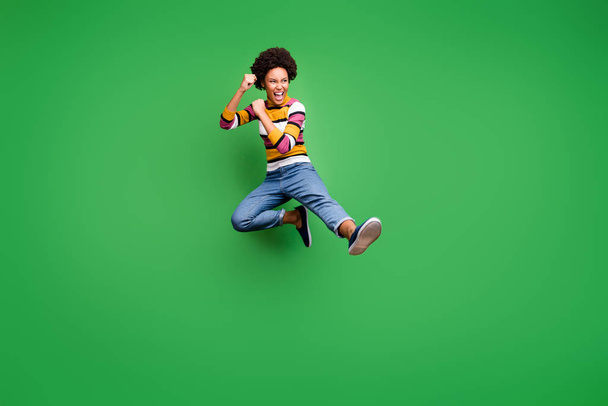 Full length photo of crazy afro american girl hipster jump train kickboxing fight copyspace fall sport kick legs fists wear trendy denim jeans isolated over green color background - Photo, image