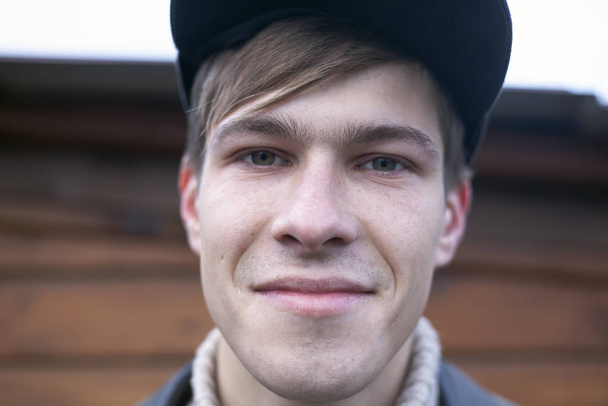 21-23 éves férfi egy sapkában mosolyog a kamerába, portré közelkép - Fotó, kép