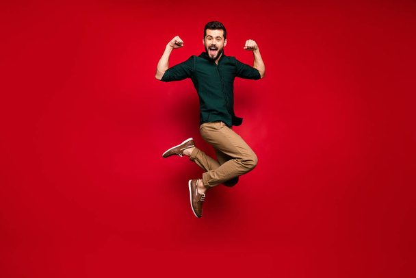 Full body photo of cheerful guy jump show his power musclar hands triceps win sport contest scream feel crazy expression wear green brown shirt sneakers isolated shine color background - Photo, image