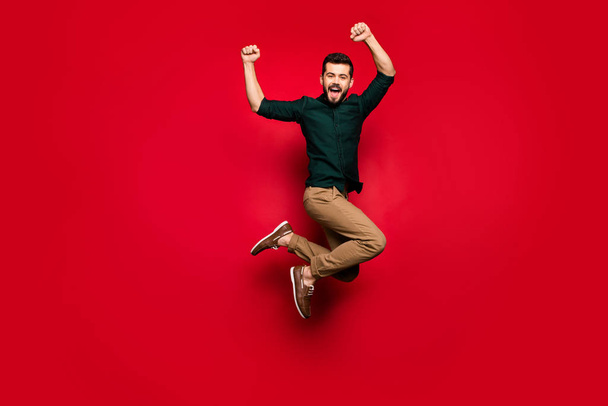 Full length photo o0f delighted guy celebrate lottery victory jump raise fists scream yes wear brown pants trousers isolated over red color background - Zdjęcie, obraz