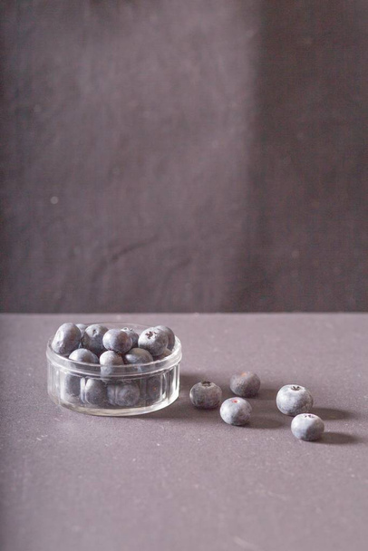 A vertical shot of berries in a small container and other five berries placed in a brown surface with a blurred background - Fotografie, Obrázek