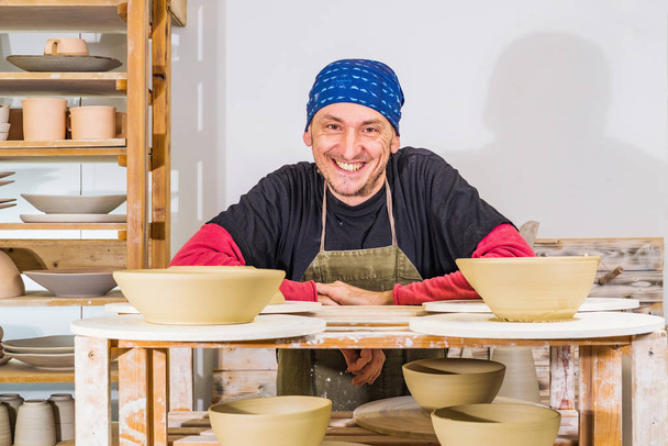 Happy successful potter in studio posing and smiling behind shelves with his products, small art business concept - Photo, Image