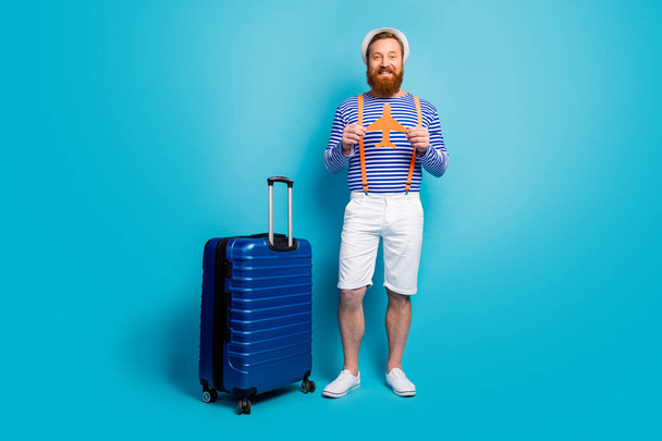 Full body photo positive man hold papercard plane ready go check in enjoy summer voyage weekend have trolleys wear white shorts orange suspenders headwear isolated blue color background - Fotografie, Obrázek