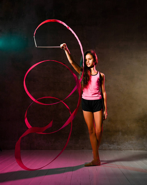 Slim athletic girl teenager gymnast with long curly hair is doing rhythmic gymnastic exercises with tape, doing spiral - Fotó, kép
