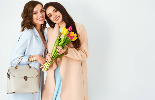 Women with spring flower bouquet. Two beautiful girls in fashion stylish clothes posing and smiling.  Spring girls with flowers. Happy women's day. March 8. - Photo, image