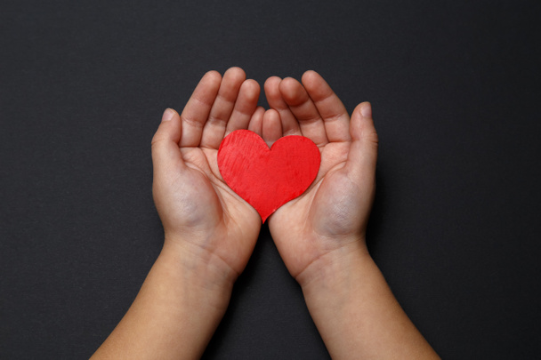 Children's hands hold a red heart on a black background, healthcare, love, organ donation, family insurance and CSR concept, World Heart Day, World Health Day, World Volunteer Day. - Fotoğraf, Görsel