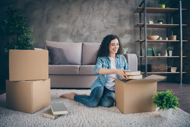 Nice attractive lovely cheerful cheery wavy-haired girl sitting on floor carpet opening unwrapping unpacking her own things in modern loft industrial style interior living-room - Fotó, kép