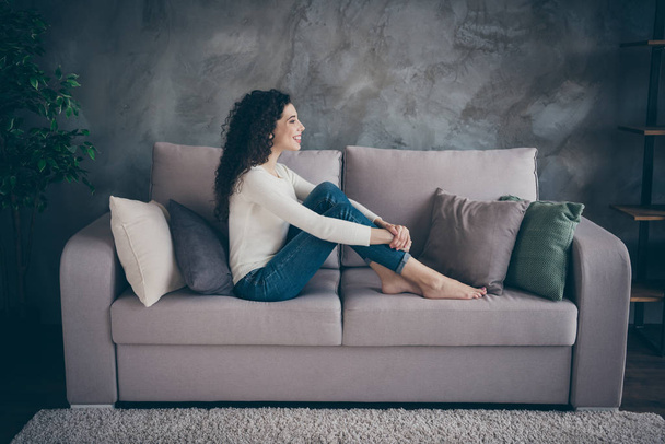 Profile side view of her she nice-looking attractive sweet lovely cheerful cheery wavy-haired girl sitting on divan spending day in modern loft industrial style interior living-room indoors - Foto, Imagem