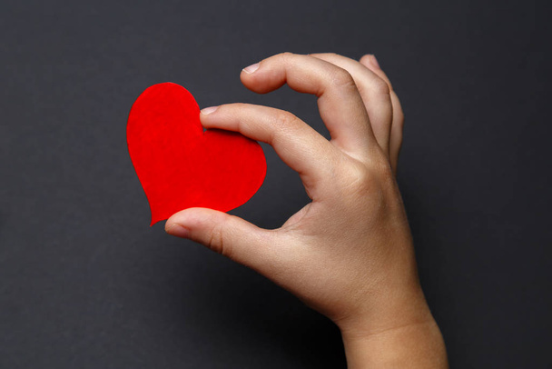 Children 's hands hold a red heart on a black background, healthcare, love, organ donation, family insurance and CSR concept, World Heart Day, World Health Day, World Volunteer Day
. - Фото, изображение