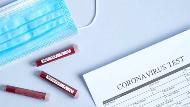 Coronavirus blood test concept. Medical form Coronavirus test, respiratory mask and test tubes with blood on desk in laboratory. 2019-nCoV biochemical analysis. Chinese Wuhan virus outbreak - Foto, Imagen