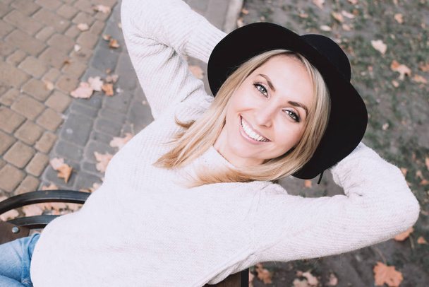 Portrait of a young woman in white sweater and black felt hat on the autumn leaves background. - Foto, Bild