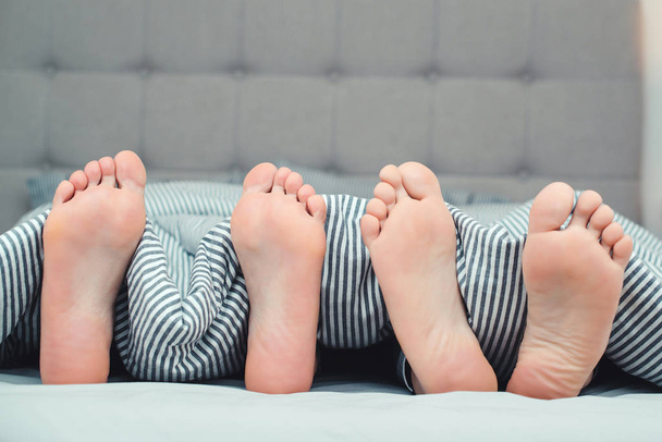 Os pés de um jovem casal na cama, de perto. Namorado e namorada deitados na cama debaixo do cobertor. Quarto de família
 - Foto, Imagem