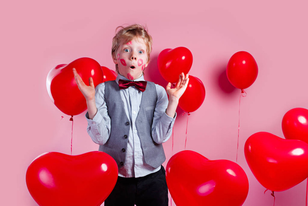 Surprised funny little boy in red balloons in the shape of a heart - Fotografie, Obrázek