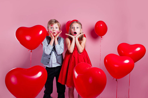 Surprised little boy with red kisses on the skin and girl in red balloons on pink background - Photo, image