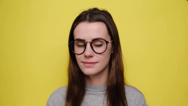 Young woman zips her mouth shut, promises to keep secret, holds fingers near cheek, makes promise, hides information dressed in grey t-shirt, isolated over yellow background. Keeping quiet concept - Video