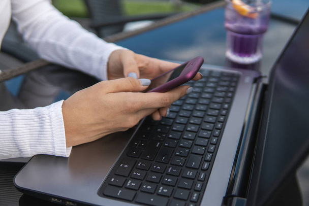 現代のビジネス女性は、ノートパソコンでカフェに座っている間、スマートフォンで着信SMSメッセージを読んだり、現代の携帯電話でオンラインで放送を見ています。女子学生コーヒーに座って. - 写真・画像