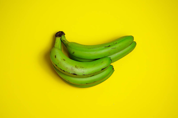 黄色の背景に緑のバナナ。醜い食べ物の概念。ミニマリズムの概念. - 写真・画像