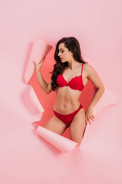 sensual girl in red lingerie standing in paper hole on pink background - Photo, Image