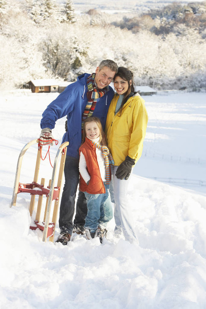 Young Family Standing In Snowy Landscape Holding Sledge - Foto, immagini
