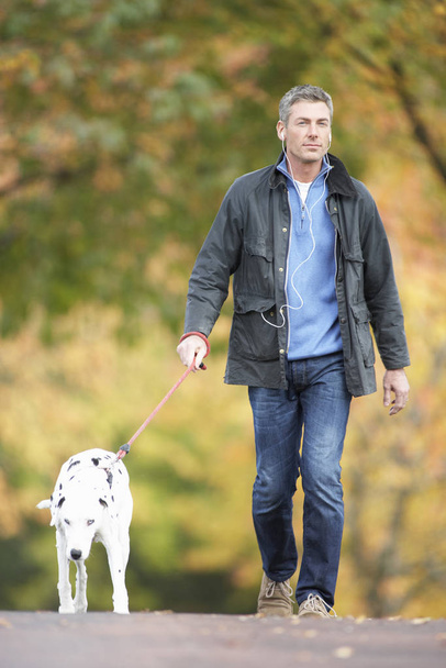 Man Walking Dog Through Autumn Park Listening to MP3 Player - Foto, afbeelding