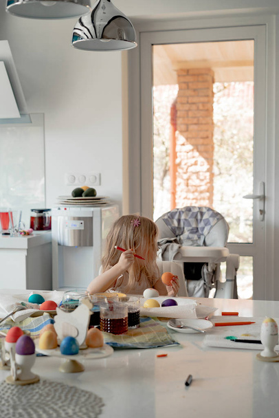 Mother and her daughters painting eggs. Happy family preparing for Easter. - 写真・画像