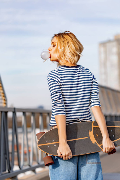 Urban stylish young girl walking with skateboard. Outdoors portr - Valokuva, kuva