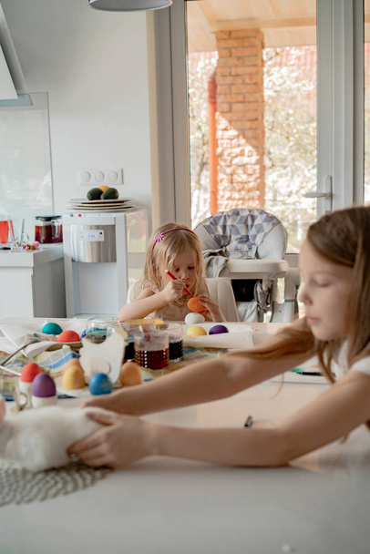 Mother and her daughters painting eggs. Happy family preparing for Easter. - Foto, afbeelding