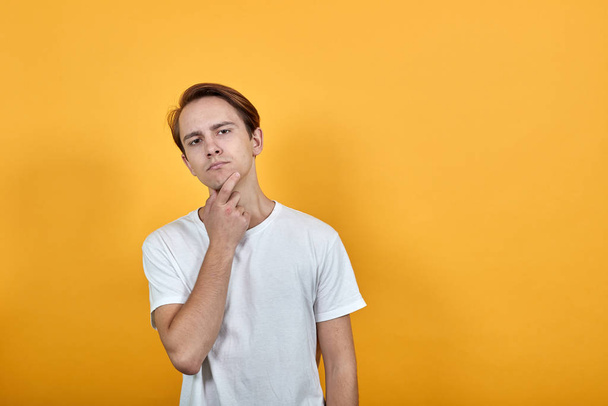 white t-shirt yellow background brunette man shows fingers on acne on his face - Foto, immagini