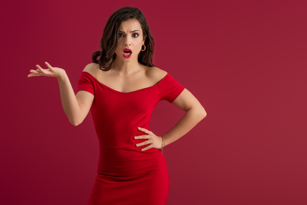 irritated, elegant girl screaming at camera while standing with open arm isolated on red - Photo, Image
