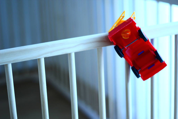 Kleine brandweerman plastic baby speelgoed auto op een houten kinderbedje. Om te spelen. Voor de lol. - Foto, afbeelding