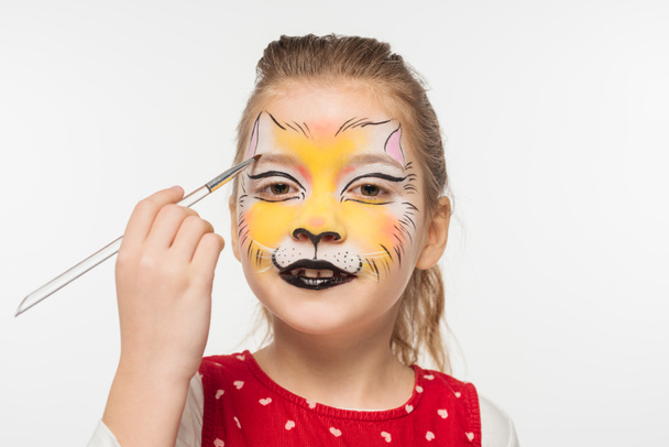 schattig kind met tijger muilkorf geschilderd op gezicht schilderij op wenkbrauw met paintbrush geïsoleerd op wit - Foto, afbeelding
