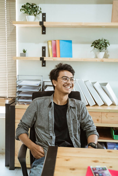 smiling young asian entrepreneur when sitting on desk - Photo, Image