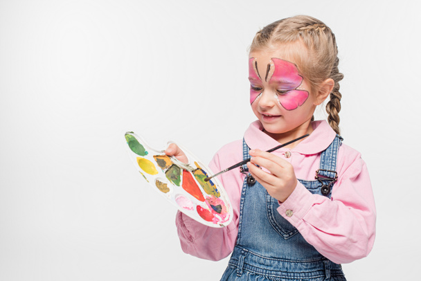 adorable child with butterfly painting on face holding palette and paintbrush isolated on white - Photo, Image