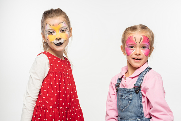 adorable children with cat muzzle and butterfly paintings on faces looking at camera isolated on white - Fotoğraf, Görsel