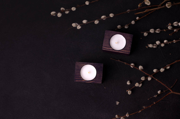 candles in a wooden candlestick next to willow branches on a black background.Dark style with copy space - Photo, image