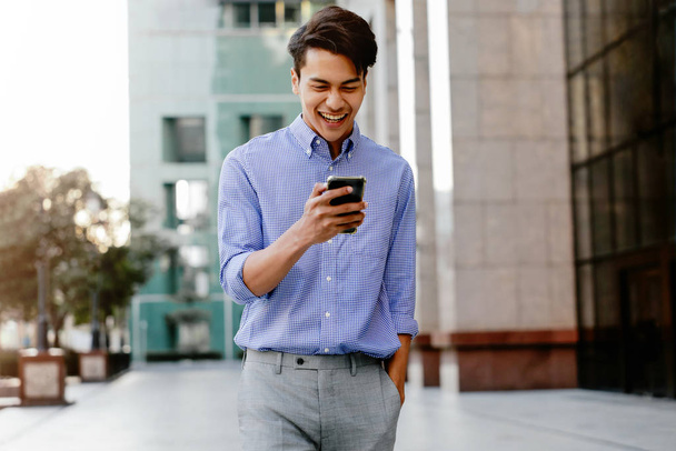 Portrét šťastného mladého podnikatele používajícího mobilní telefon v městském městě. Životní styl moderních lidí. Přední pohled. Moderní budova jako pozadí - Fotografie, Obrázek