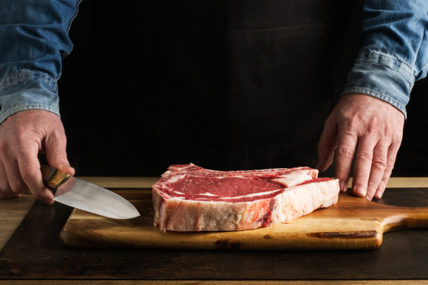 Homme avec un couteau à la main et un t-bone sur une planche de cuisine en bois
 - Photo, image