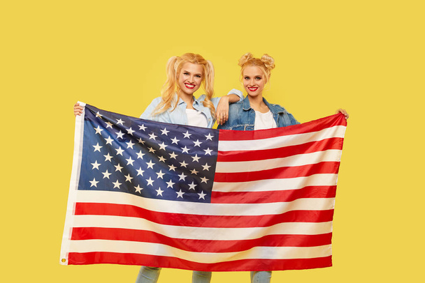 American girls. Happy young women in denim clothes holding USA flag isolated on yellow background. football fan - Фото, зображення