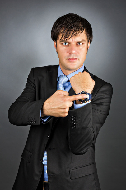 Jovem empresário apontando para seu relógio com uma expressão irritada
 - Foto, Imagem