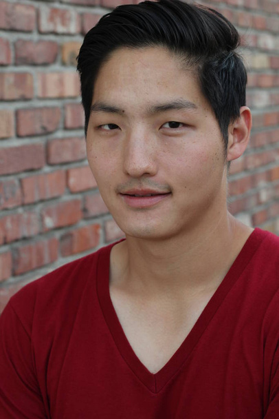 close-up portrait of handsome young asian man in casual clothes in front of brick wall - Photo, Image