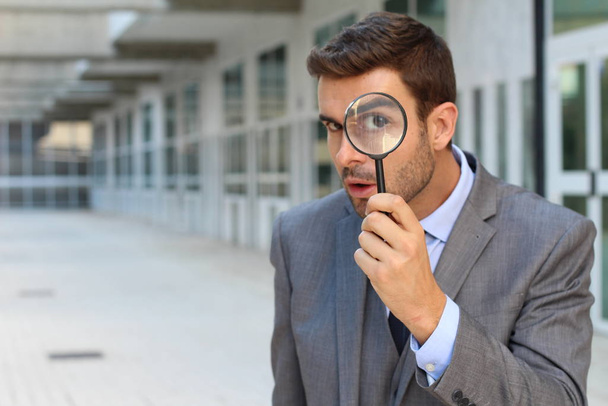 close-up portrait of handsome young businessman with magnifying glass on street - Photo, Image