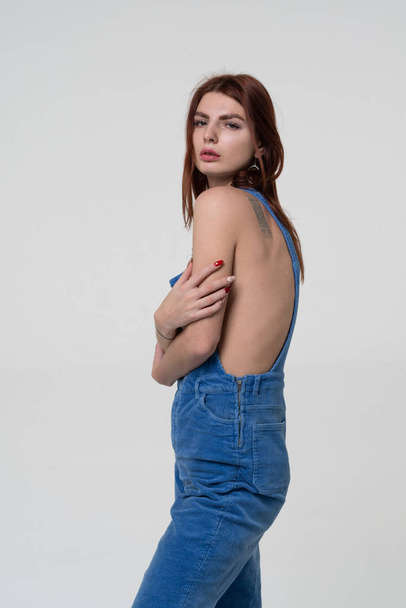 young beautiful girl stands in blue overalls - Φωτογραφία, εικόνα