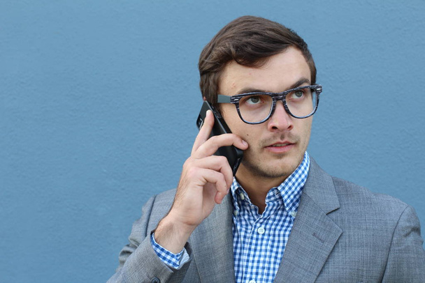 Mavi duvarın önünde telefonla konuşan yakışıklı genç iş adamının yakın plan portresi. - Fotoğraf, Görsel