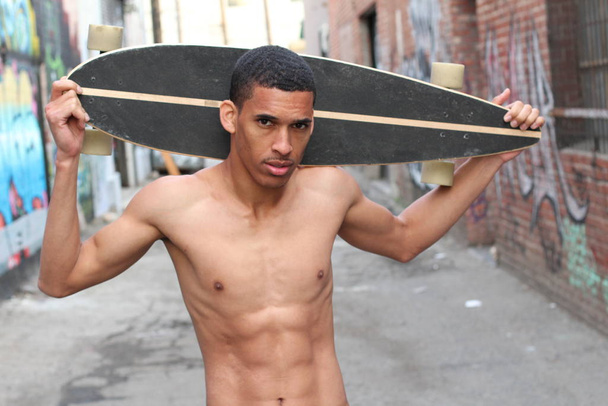 Nahaufnahme Porträt eines hübschen jungen Afroamerikaners ohne Hemd mit Longboard auf der Straße - Foto, Bild
