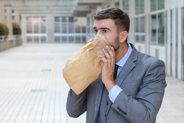 close-up portrait of stressed young businessman breathing with paper bag - Photo, Image