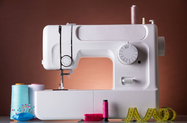 The workplace of seamstress. White electric sewing machine on a brown background and accessories for sewing - Φωτογραφία, εικόνα