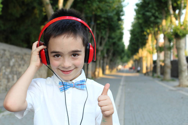 Портрет стильного мальчика в красных наушниках, стоящего на улице  - Фото, изображение