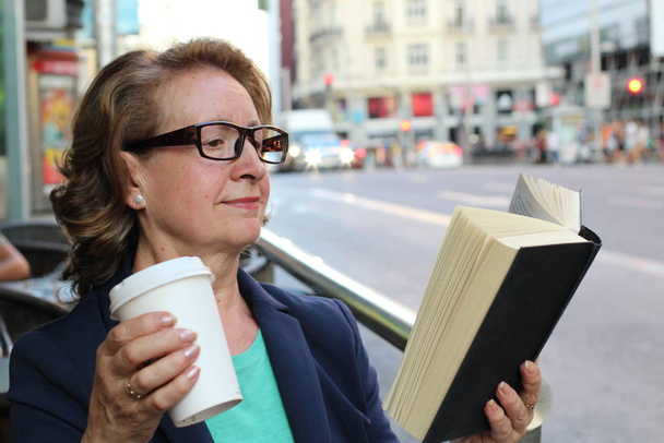 Kypsä nainen juo kahvia ja lukee kirjaa istuu sisällä kaupunkien kahvilassa. Cafe kaupunki elämäntapa liikennevalot taustalla
 - Valokuva, kuva